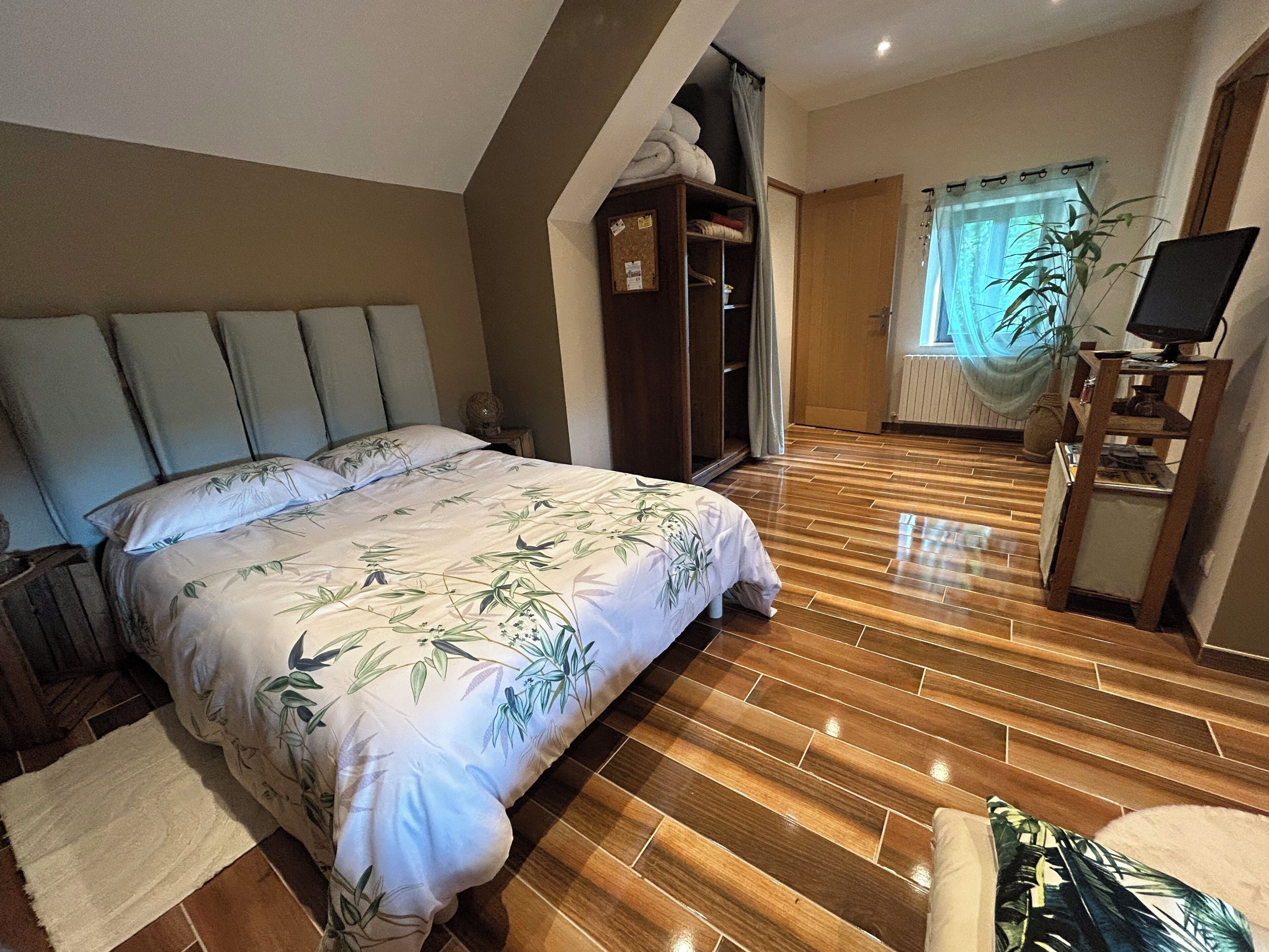 Ein Schlafzimmer mit Bett, Holzboden, Kleiderschrank, Fernseher und einem Fenster mit Vorhängen.