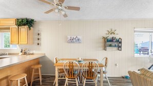 Eine Küche mit Holzausstattung, einem Esstisch mit vier Stühlen, einem Deckenventilator und einem Fenster mit Blick auf ein Haus.