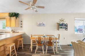 Eine Küche mit Holzausstattung, einem Esstisch mit vier Stühlen, einem Deckenventilator und einem Fenster mit Blick auf ein Haus.
