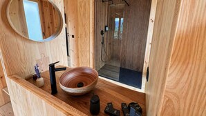 Ein Badezimmer einer Holzhütte mit einem runden Spiegel, einem Holzbecken, einem schwarzen Wasserhahn, einem schwarzen Seifenspender und einem schwarzen Zahnbügelhalter.