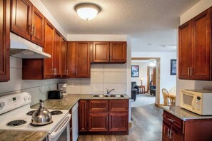 A kitchen with wooden cabinets, a stove, a microwave, and a sink. - 4-Bedroom Apartment at Blue Mountain · Walk to Village · Private Beach Access (Collingwood)