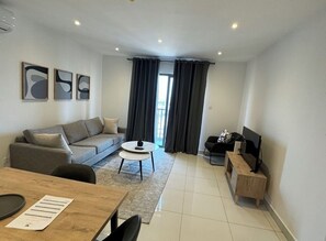 Ein modernes Wohnzimmer mit Sofa, Couchtisch, TV-Standfuß und einem Essbereich mit Tisch und Stühlen.