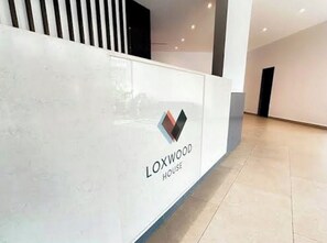Eine Rezeption mit dem Logo 'LOXWOOD HOUSE' und einem modernen Innenraum mit Fliesenboden.
