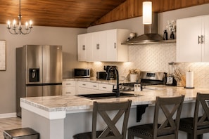 Une cuisine moderne dotée d’appareils électroménagers en acier inoxydable, de meubles blancs, d’un îlot en marbre et d’un plafond en bois.