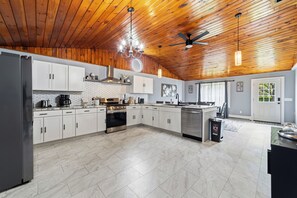 A spacious kitchen with white cabinets, a stainless steel refrigerator, a built-in oven, and a ceiling fan.