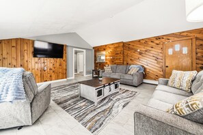 Un salon moderne avec un lambris en bois, un téléviseur à écran plat, des canapés gris et une table basse.