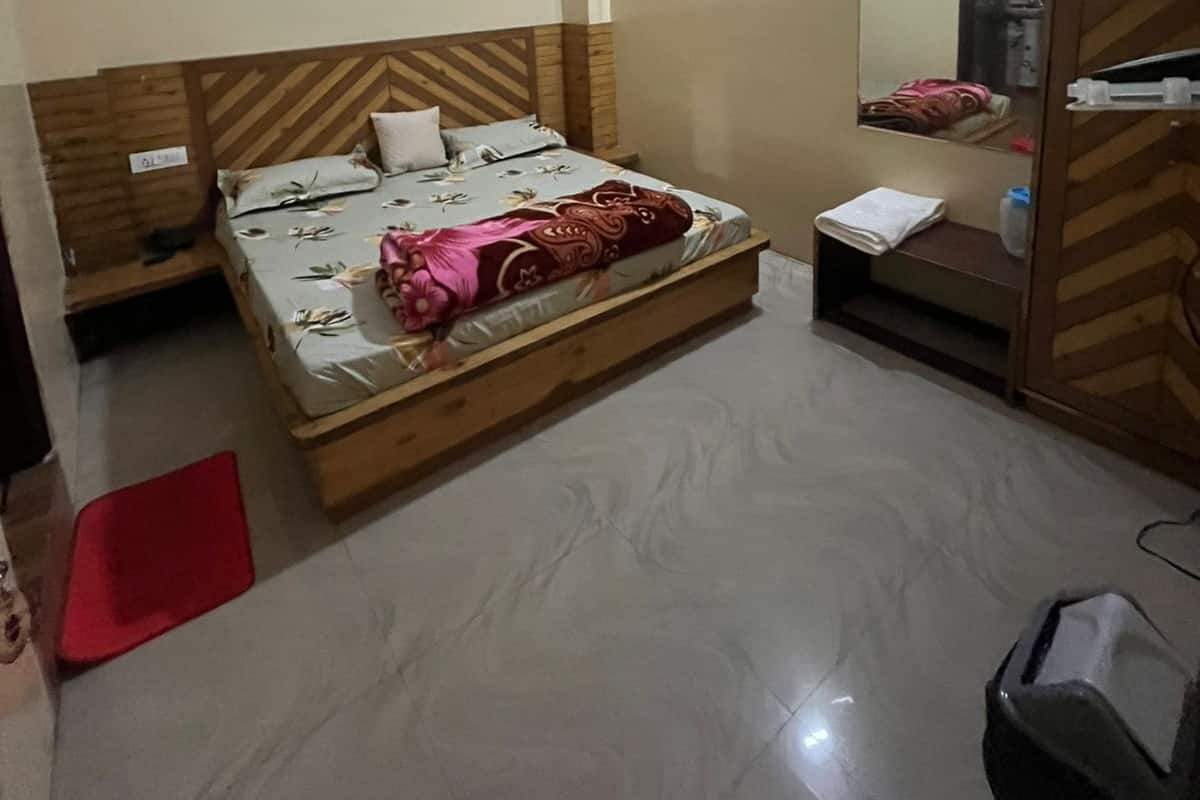 A bedroom with a wooden headboard, a bed with a floral bedspread, a bedside table, a mirror, and a wardrobe.