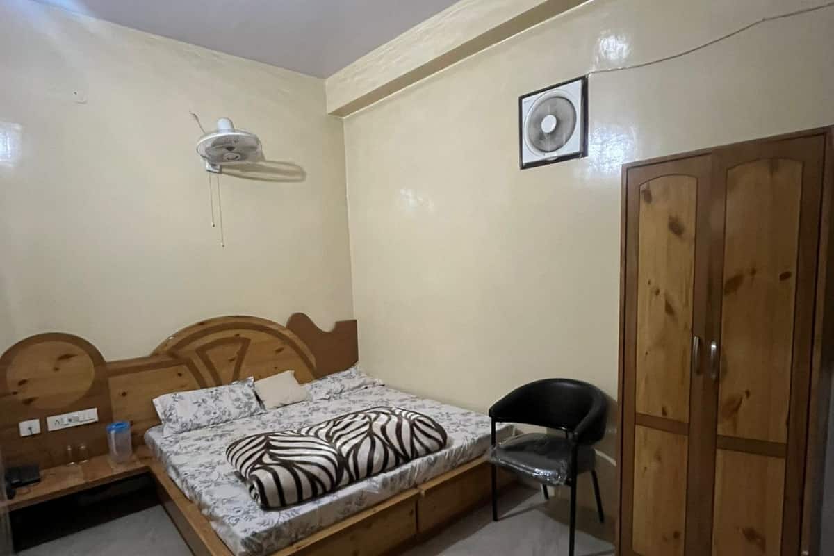 A bedroom with a bed, a wardrobe, a chair, a fan, and a wall-mounted heater.