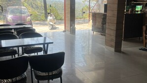A spacious indoor area with a dining table and chairs, a motorcycle outside, and a view of a mountainous landscape through large windows. - The Classic Residency Hotel & Banquet  (Shimla)