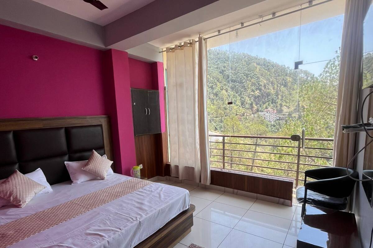 A bedroom with a bed, a ceiling fan, a balcony with a view of a green landscape, and a TV on a stand.