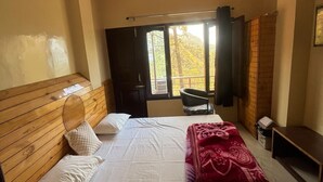 A bedroom with a wooden headboard, a bed with white linens, a red blanket, a ceiling fan, a window with a view of trees, and a small table. - The Classic Residency Hotel & Banquet  (Shimla)