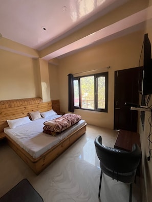 A bedroom with a bed, a desk, a chair, a TV, and a window with curtains.