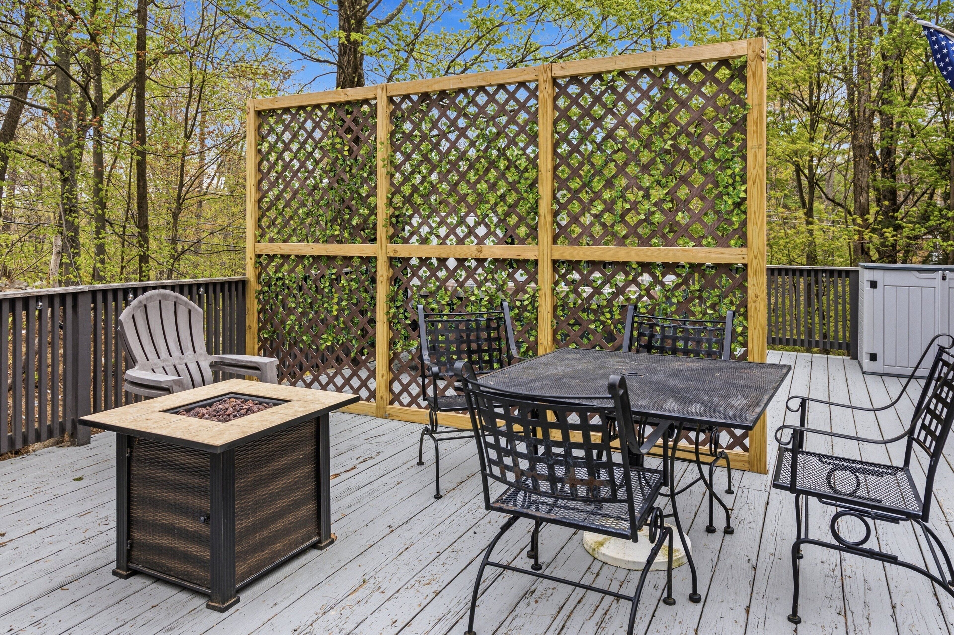 A deck with a fire pit table, chairs, and a lattice screen.