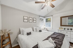 Ein Schlafzimmer mit Bett, Deckenventilator, Nachttisch, Kommode und gerahmten Wandbildern.