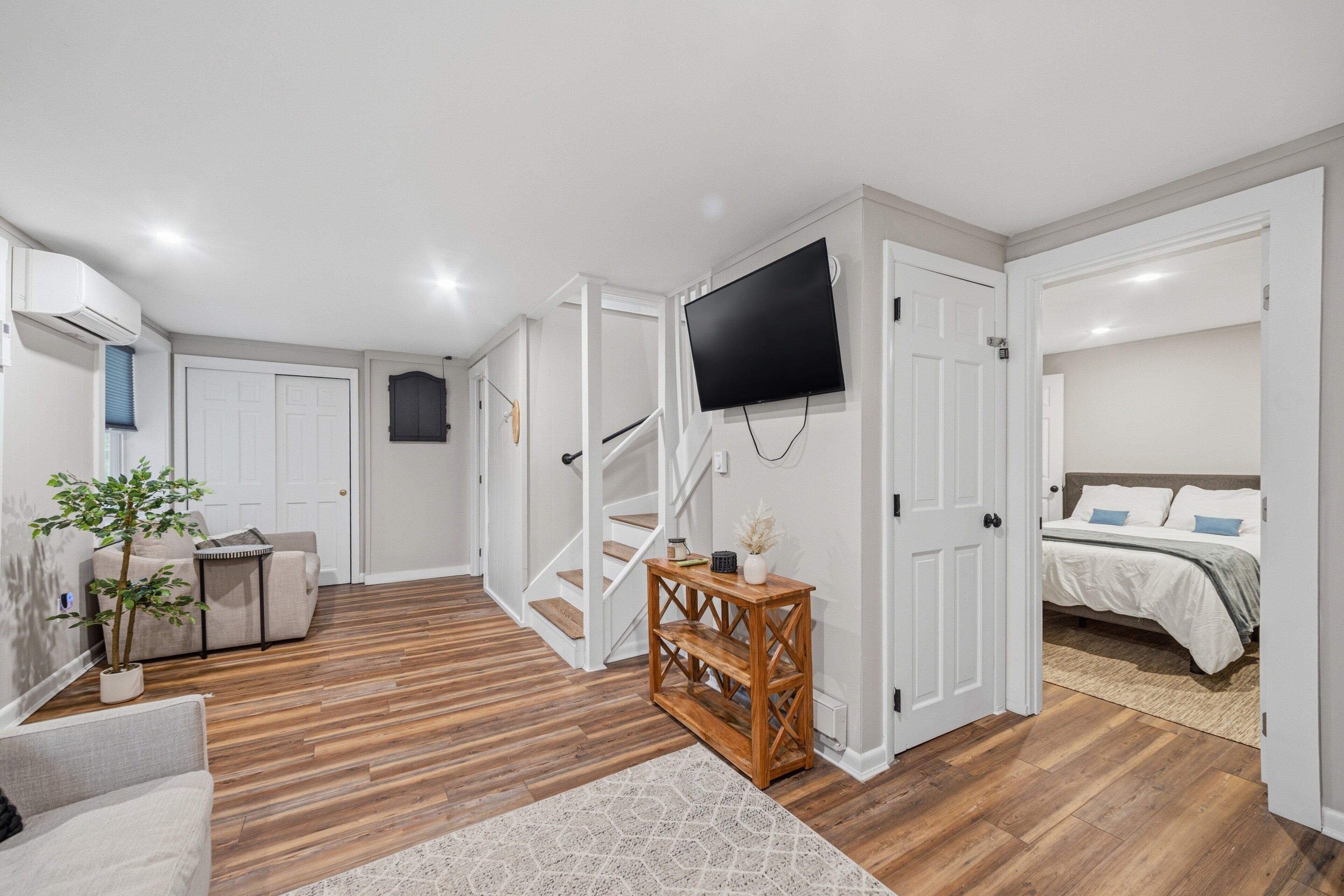 A modern interior with a staircase, a flat-screen TV mounted on the wall, a sofa, and a bed.
