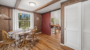 A dining area with a wooden table and chairs, a red door, and a view of greenery outside. - Forest Chalet With Hot Tub Near Gunstock 3 Bedroom Home (Gilford)