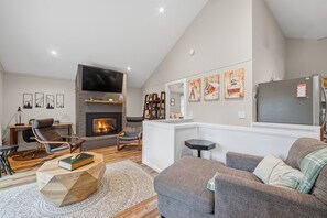 Ein Wohnzimmer mit Kamin, Flachbildfernseher, einer Couch, einem Couchtisch und einem Bücherregal.