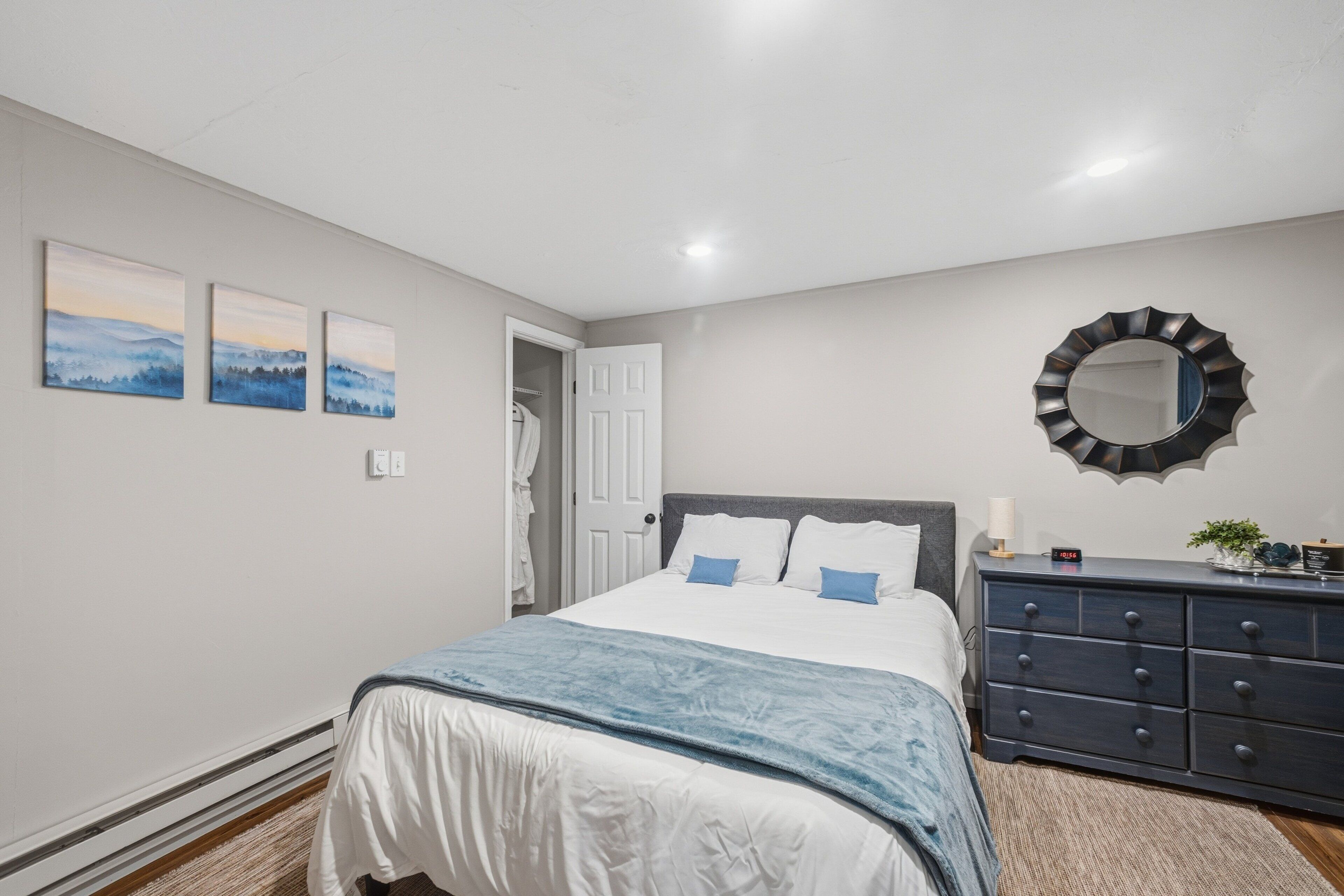 A bedroom with a bed, a dresser, a mirror, and three paintings on the wall.