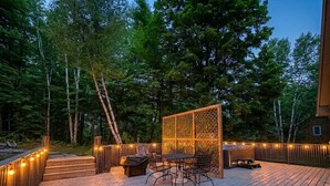 A wooden deck with outdoor furniture, a lattice screen, and string lights. - Forest Chalet With Hot Tub Near Gunstock 3 Bedroom Home (Gilford)