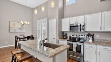 A kitchen with white cabinets, a granite countertop, stainless steel appliances, and a dining area with wooden chairs and a table.