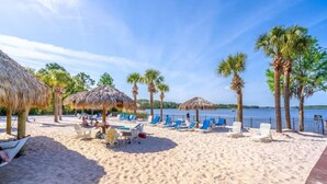 Ein Strand mit Liegestühlen, Reetdachschirmen und Palmen.