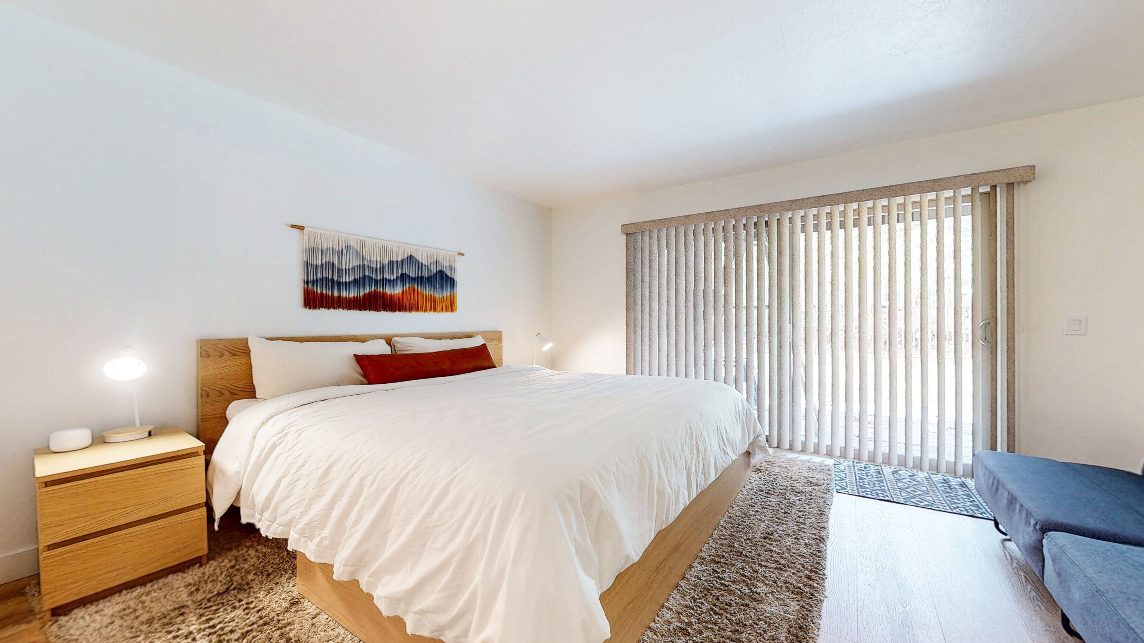 Une chambre à coucher moderne comprenant un lit, des tables de chevet, une commode, une lampe fixée au mur, une fenêtre avec des stores et un élément décoratif mural.
