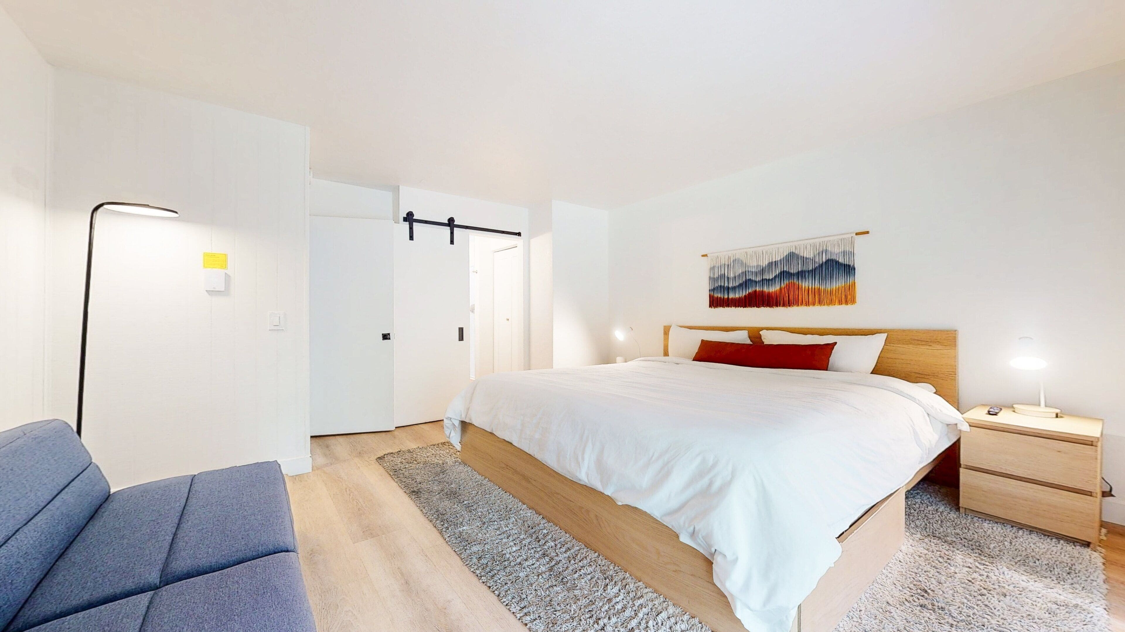 Et moderne hotelværelse med seng, natbord, lampe og en blå stol.