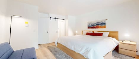 Et moderne hotelværelse med seng, natbord, lampe og en blå stol.
