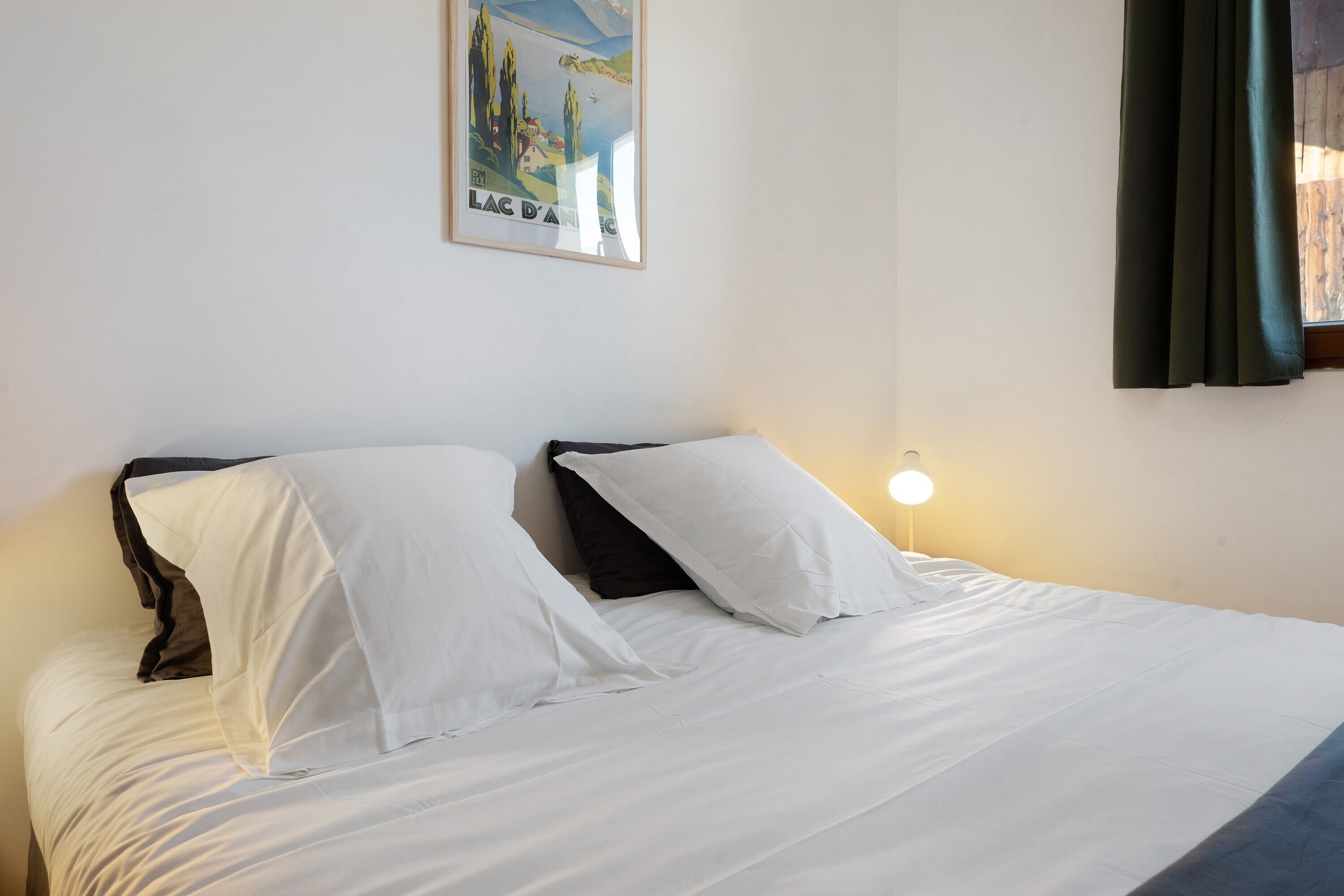 A bed with white and black bedding, a wall-mounted light, and a framed picture.