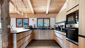 A modern kitchen with wooden cabinets, a built-in oven, and pendant lighting. - l'Hermine: Stunning Savoyard Chalet with Panoramic Views – Up to 15 Guests (La Plagne-Tarentaise)