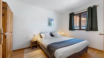 A bedroom with a bed, bedside tables, a wooden wardrobe, a window with curtains, and a wall-mounted picture.