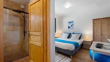 A hotel room with a shower, a bed with a blue bedspread, a desk with a computer, and a wooden wardrobe.