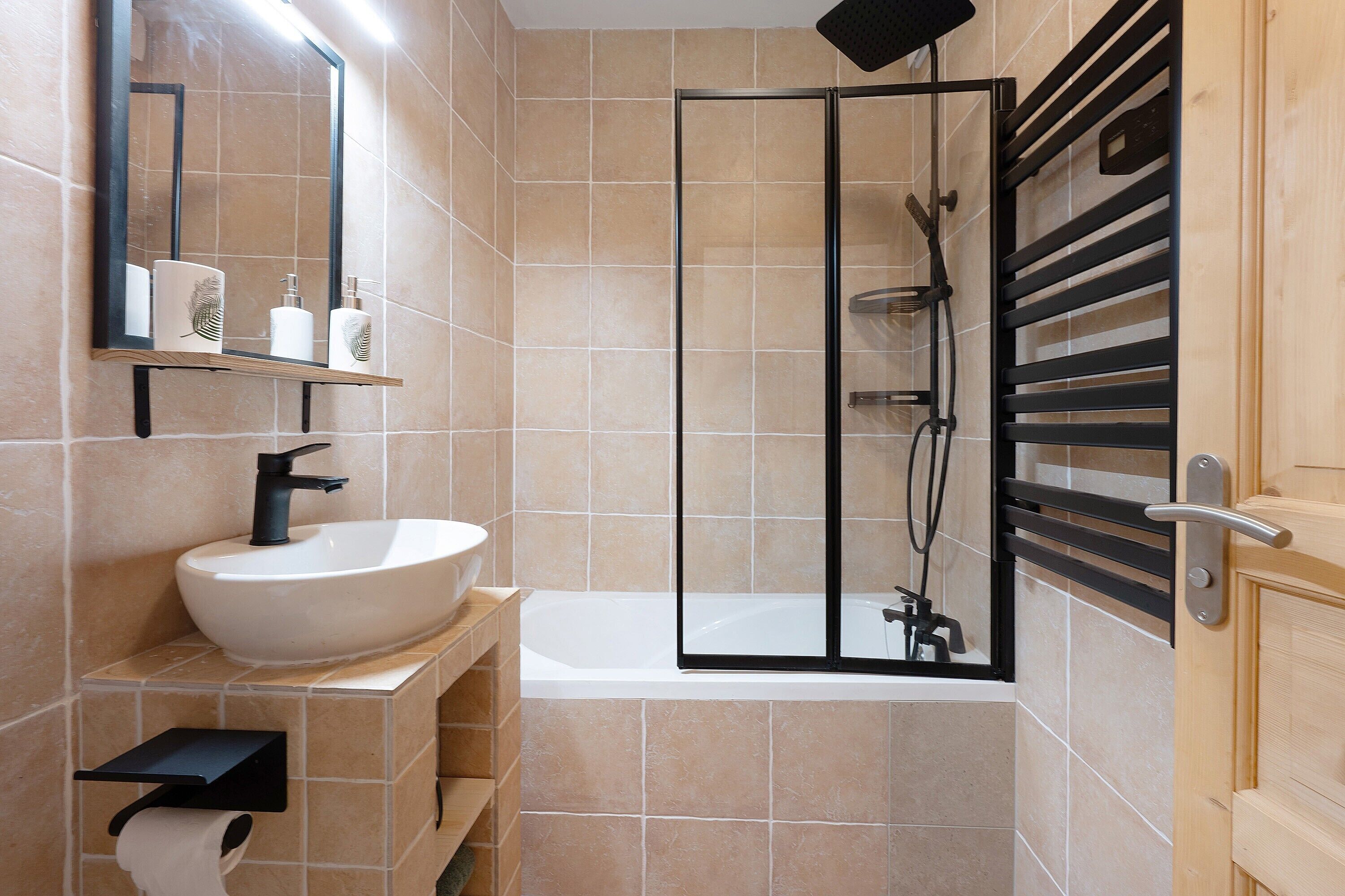 A bathroom with a sink, mirror, toilet paper holder, and a shower enclosure.