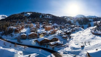 Ein verschneiter Ferienort mit mehreren Holzhäusern, Skipisten und blauem Himmel.