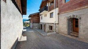 A narrow street with buildings featuring wooden facades and stone foundations. - l'Hermine: Stunning Savoyard Chalet with Panoramic Views – Up to 15 Guests (La Plagne-Tarentaise)