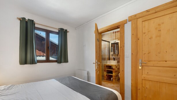 A bedroom with a bed, a window with curtains, and a wooden wardrobe. - l'Hermine: Stunning Savoyard Chalet with Panoramic Views – Up to 15 Guests (La Plagne-Tarentaise)