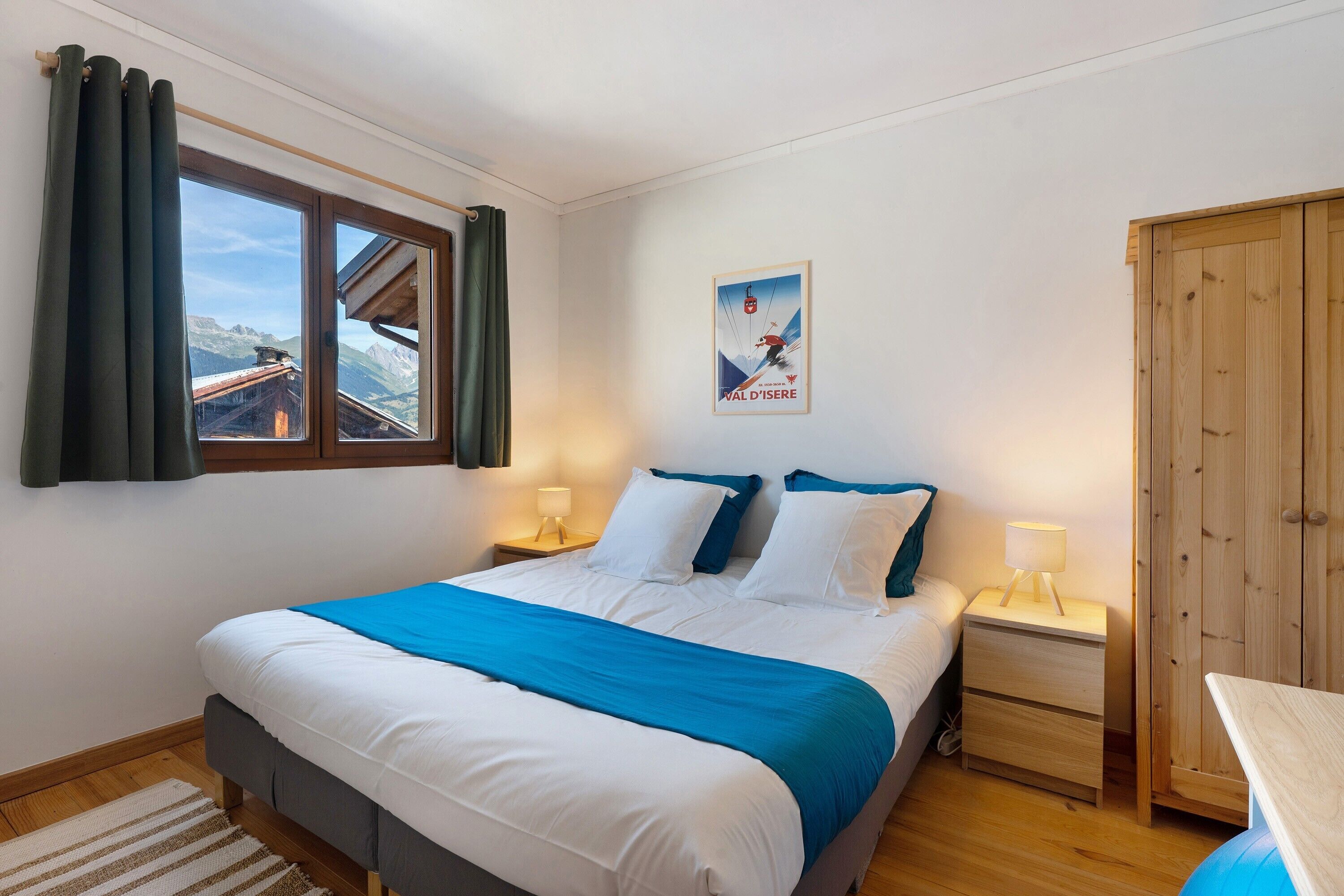 Ein Schlafzimmer mit einem Bett, einem Nachttisch, einem Holzschrank, einem Fenster mit Vorhängen und einem Poster an der Wand.