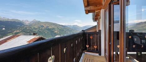 A wooden balcony with heart-shaped cutouts, overlooking a mountainous landscape.