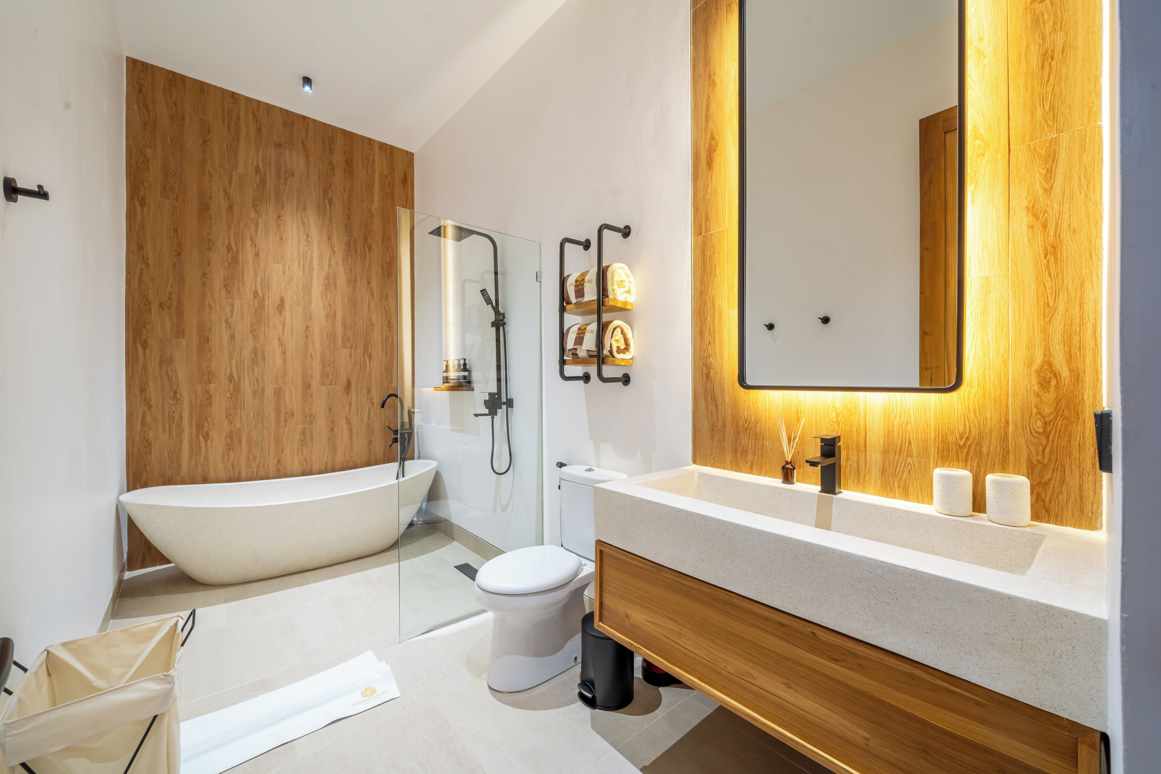 A modern bathroom with a freestanding bathtub, a toilet, a sink with a wooden vanity, and a large mirror.