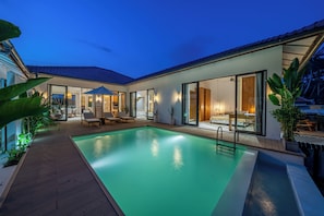 Ein modernes Haus mit Swimmingpool, großen Fenstern und Gartenmöbeln.