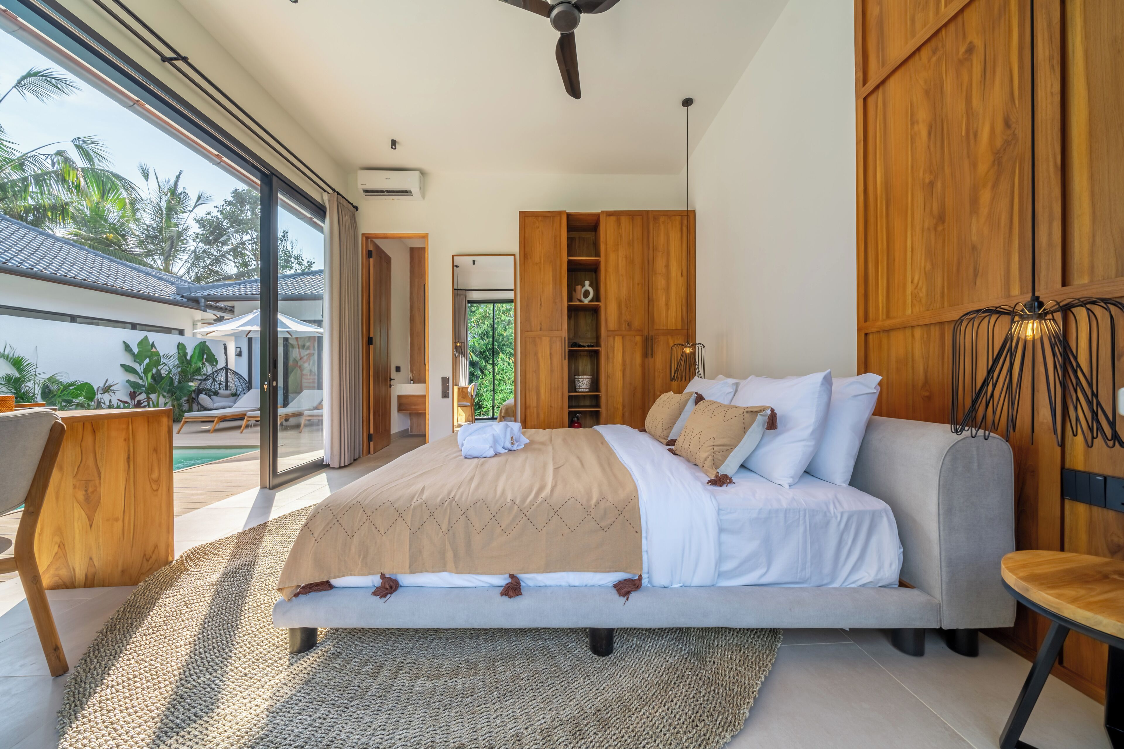 Un dormitorio con cama, sofá, armario de madera y un amplio ventanal.