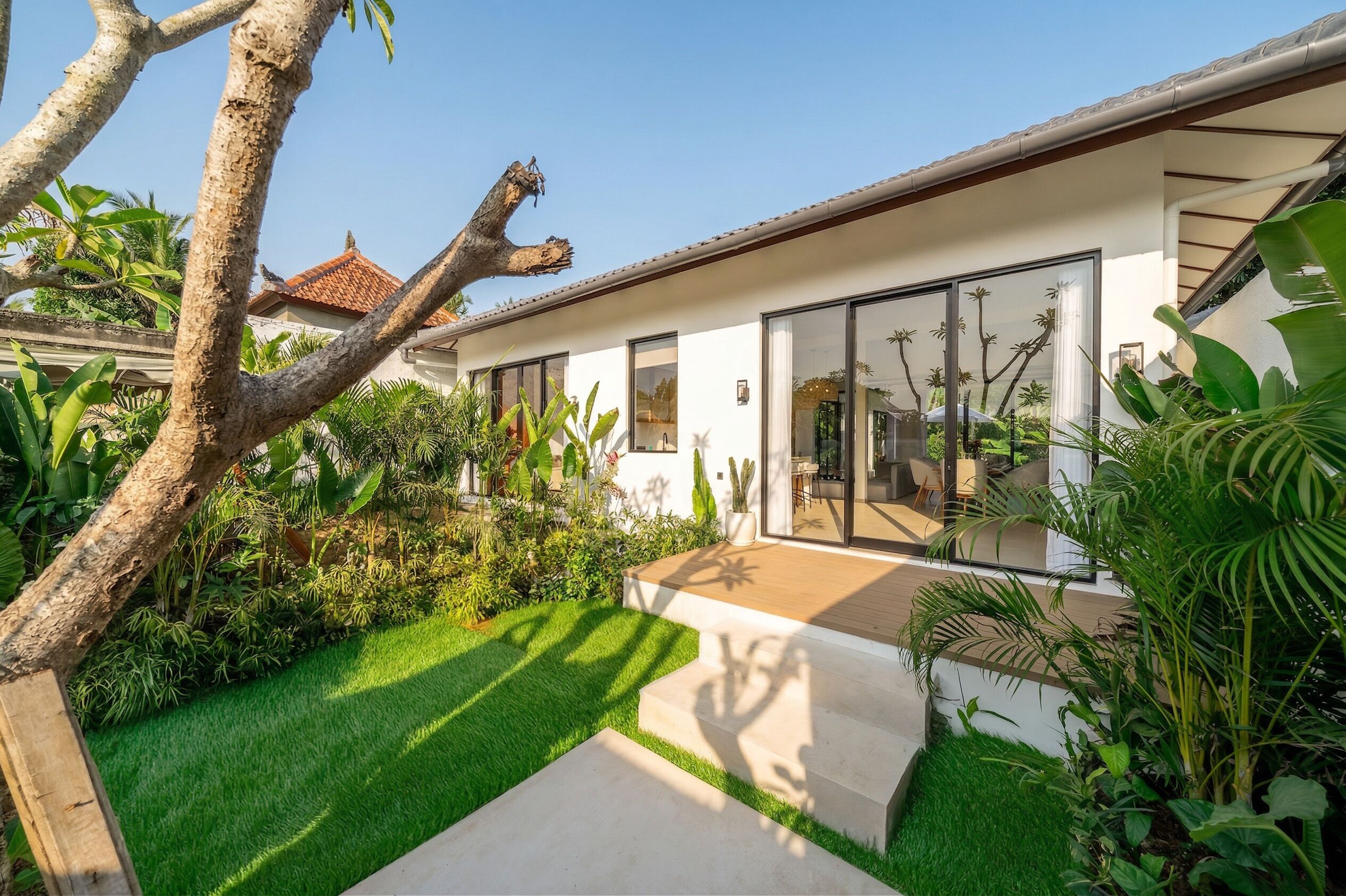 A modern house with a large glass door, a wooden deck, and lush greenery.