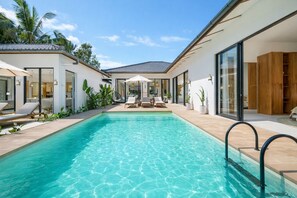Ein moderner Poolbereich mit klarem Wasser, Liegestühlen und einem gläsernen Gebäude.
