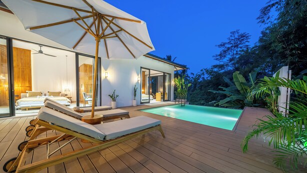 Une maison moderne dotée d’une terrasse en bois, d’une piscine et d’un grand parasol.