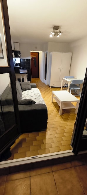 A room with a sofa, a small table, a cabinet, and a kitchenette area. - Apt 2pers, air conditioning, wifi, parkg, 10mn walk to the beach (La Grande-Motte)