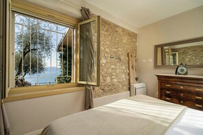 Ein Schlafzimmer mit Steinwand, einem Fenster mit Metallgitter, einem Bett, einer Kommode und einem Spiegel.