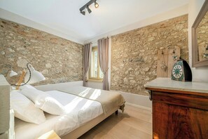 Ein Schlafzimmer mit Steinsturz, einem Bett, einer Holzkommode und einem Fenster mit Vorhängen.
