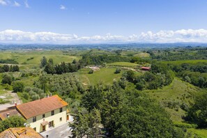 Ländliche Landschaft mit sanften Hügeln, einem kleinen Haus mit Ziegeldach und verstreuten Gebäuden.