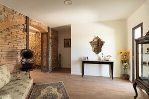 Ein Zimmer mit Backsteinwand, einem alten Grammophon, einem floralen Sofa, einem Konsolentisch mit Spiegel und einer Vase mit Sonnenblumen.