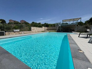 Ein rechteckiger Swimmingpool mit klarem, blauem Wasser, umgeben von einer Steinsäule und einer gepflasterten Liegefläche.